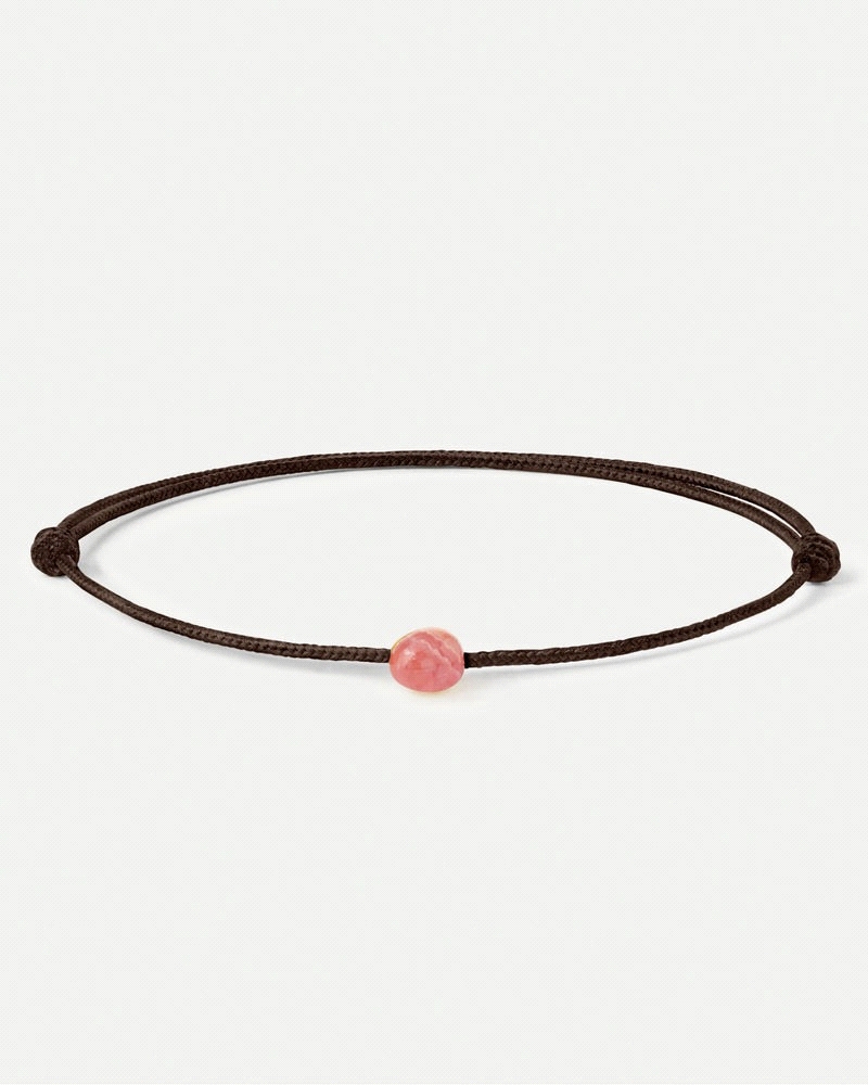 Pulsera de cordón negro ajustable con diseño de piedra rosada.